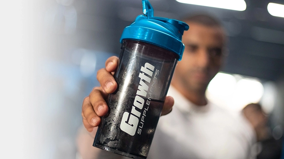Growth Supplements - mão segurando coqueteleira preta com tampa azul na academia