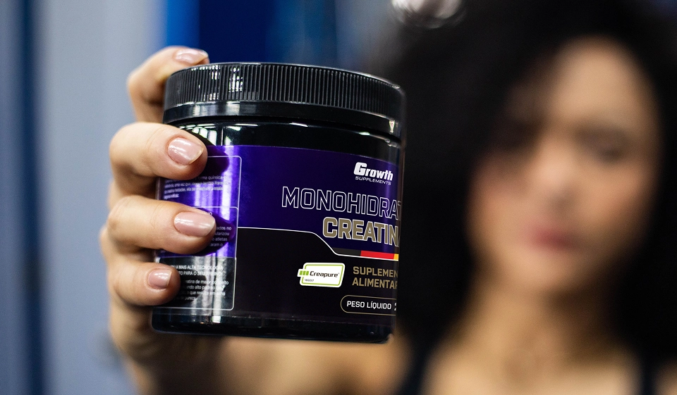 Uma mulher segurando uma creatina CreaPure 250g da Growth Supplements