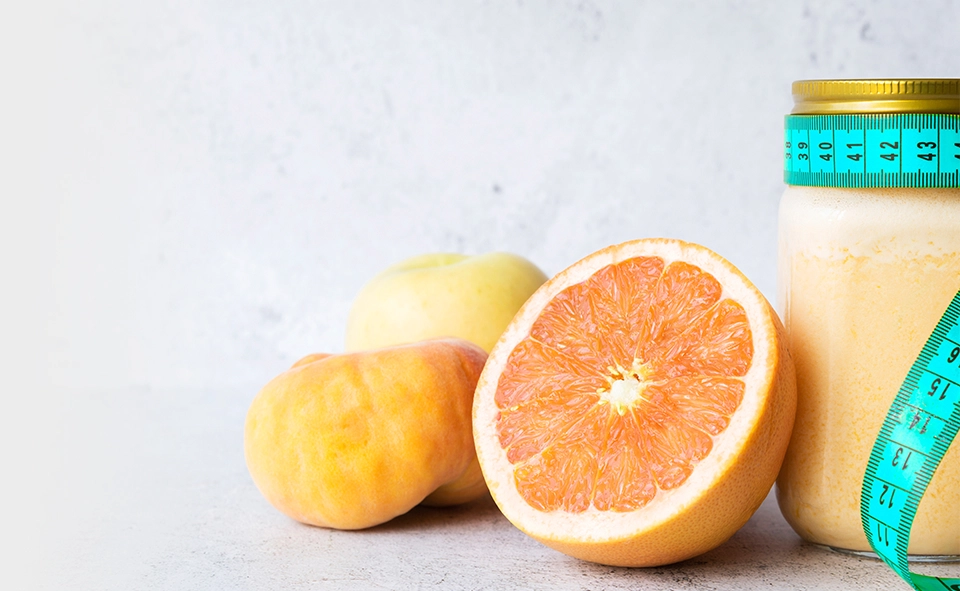 Uma laranja cortada no meio ao lado de um pote com suco dentro.