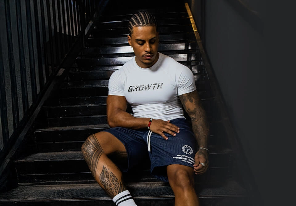 Atleta Growth Supplements sentado na escada de camiseta e shorts Growth Supplements
