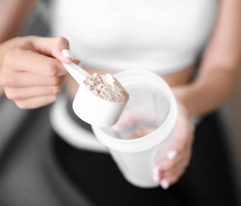 Pessoa segurando o medidor de creatina da Growth Supplements e um copo