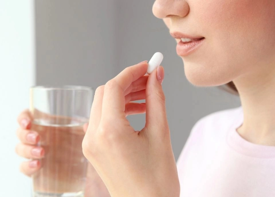 Pessoa com um copo de água e uma capsula na mão