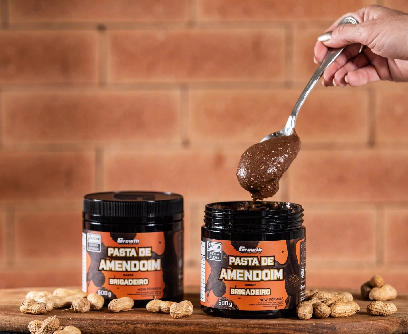 GROWTH SUPPLEMENTS - Embalagens de Pasta de Amendoim sabor brigadeiro em mesa com amendoins em volta e colher