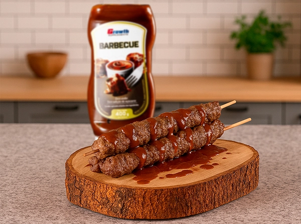 Molho barbecue Growth Supplements 400g ao lado de uma tábua de churrasco com 3 espetos em cima da mesma