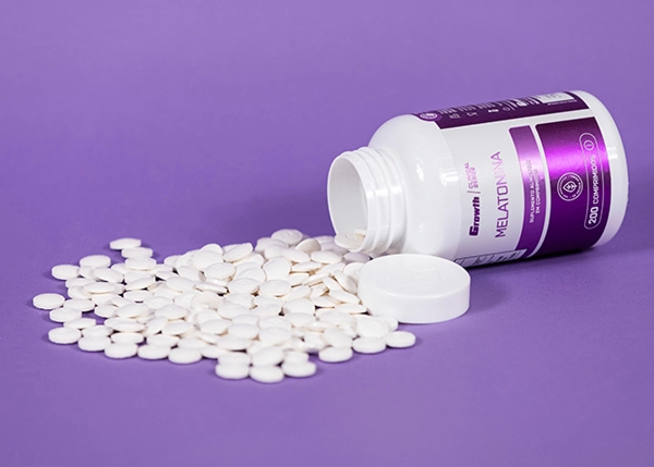 melatonina 0,21mg (200 Comprimidos) - Growth Supplements com comprimidos na frente e o fundo lilas