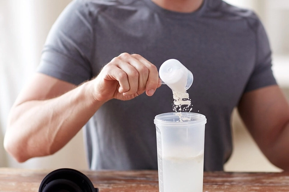 GROWTH SUPPLEMENTS - Pessoa colocando scoop de Soy Protein em coqueteleira