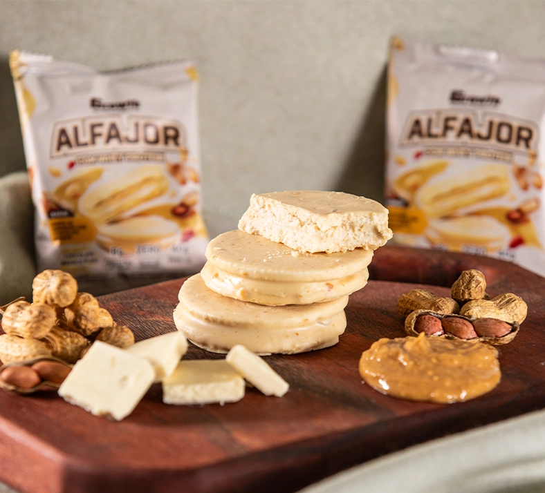 Alfajor com Whey Protein sabor chocolate branco empilhado em cima de uma tábua com duas embalagens em volta