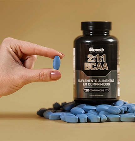 A mão de uma pessoa segurando um comprimido de BCAA 2:1:1 e um BCAA no fundo com comprimidos ao redor - growth supplements