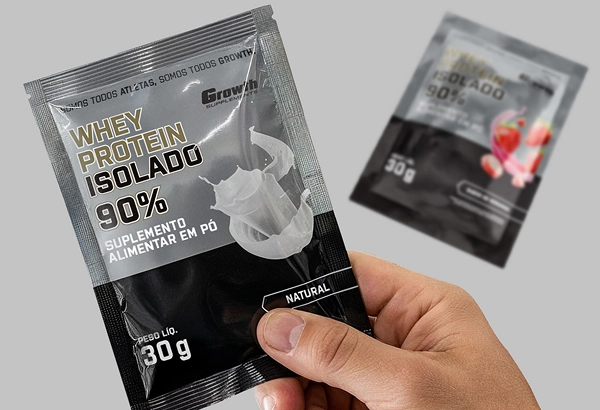 Uma mão com o sachê do Whey Isolado GROWTH SUPPLEMENTS