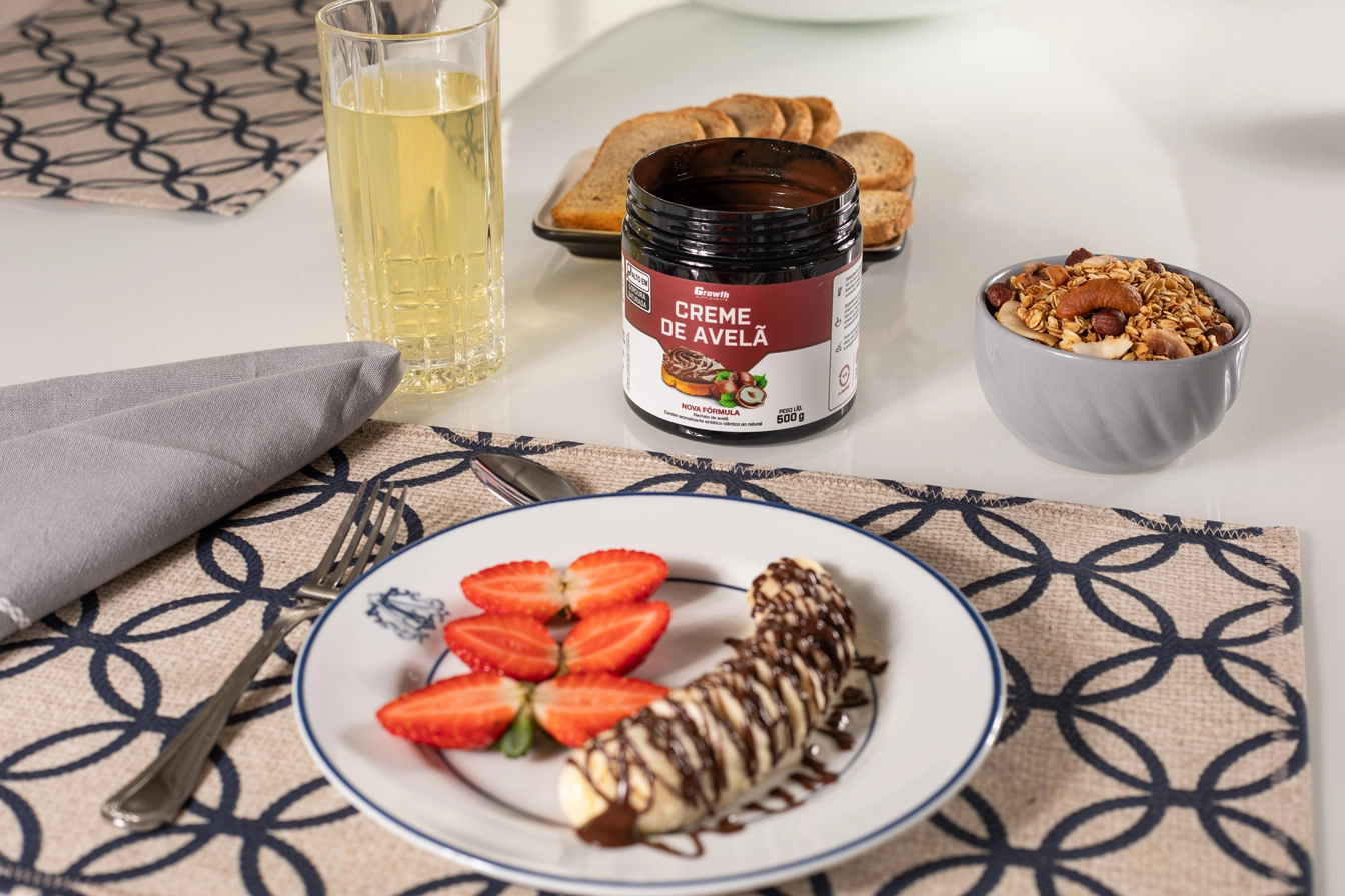 Creme de avelã Growth Supplements em cima de uma mesa com um prato com morangos e uma banana dentro